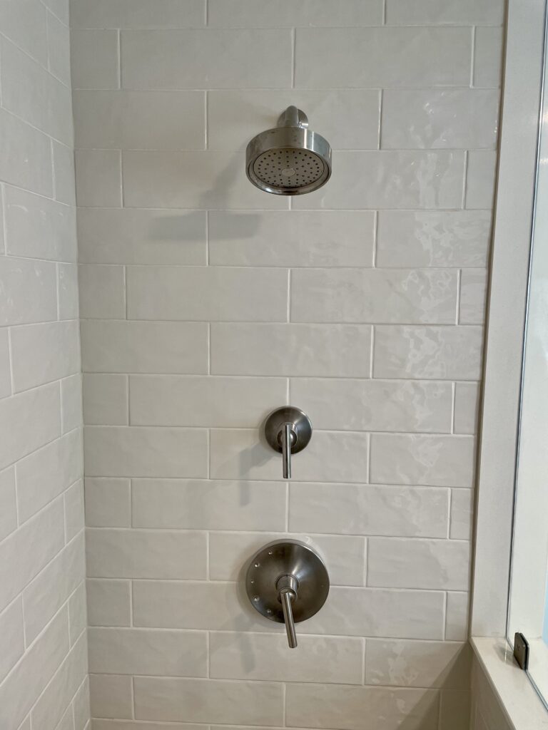 Minimalist shower setup with brushed metal fixtures and white tile wall.